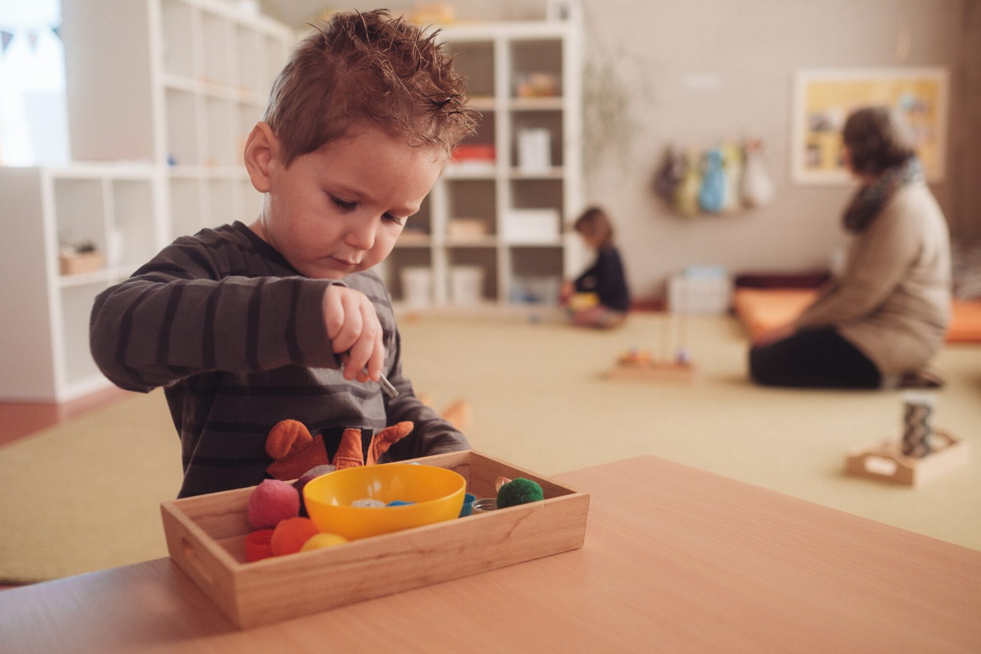 Junge sitzt alleine an einem kleinen Tisch im Montessori-Krippenraum und spielt konzentriert mit Montessori-Materialien.