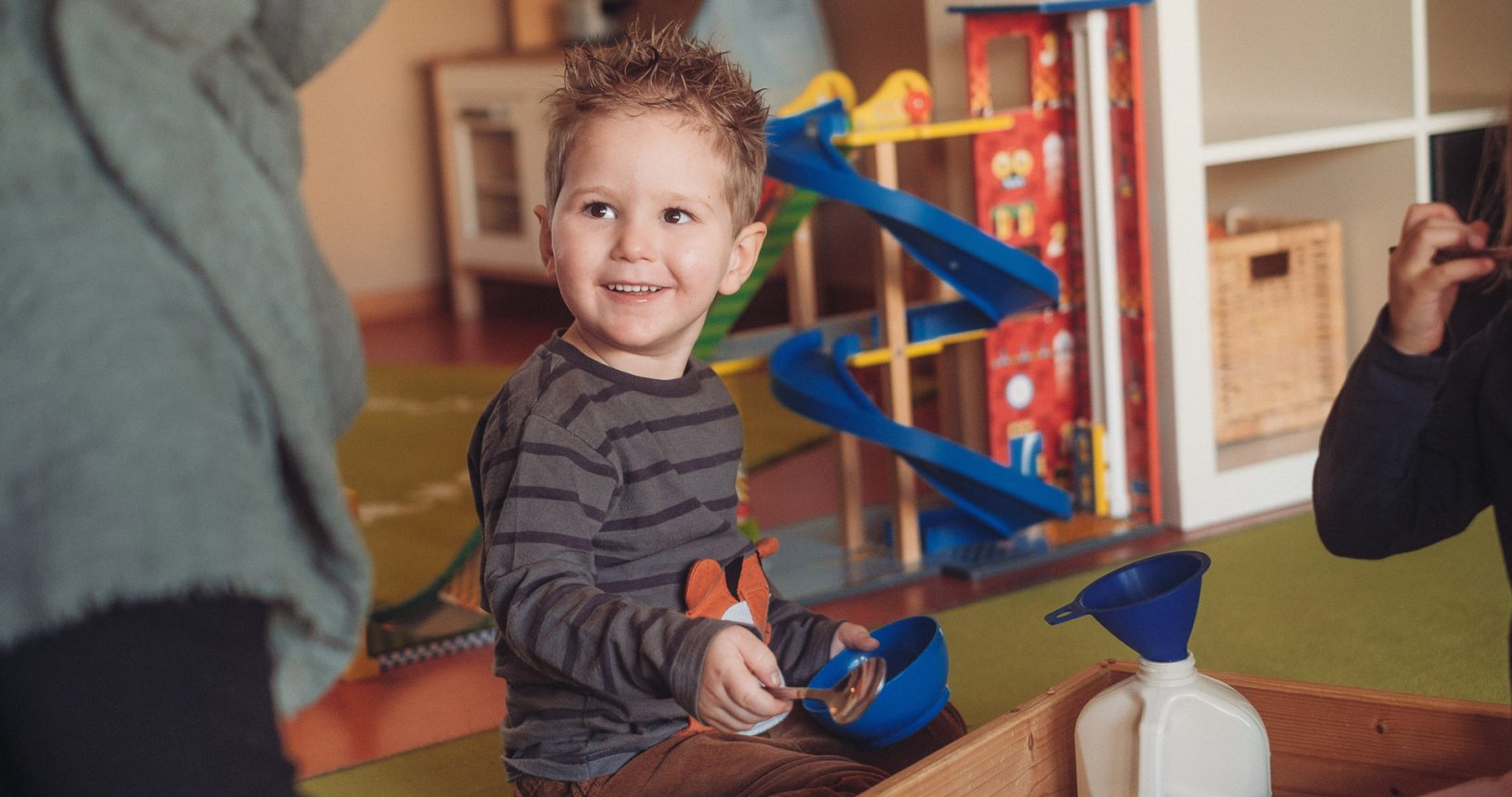 Junge spielt konzentriert auf dem Boden eines Montessori-Krippenraums mit Montessori-Spielmaterial.