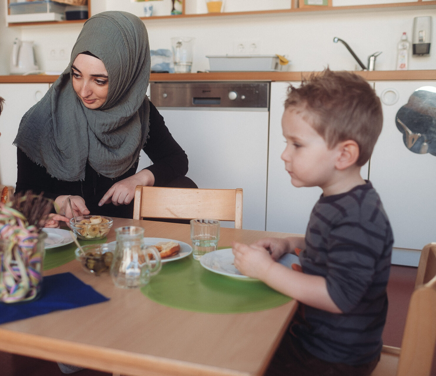 Erzieherin unterhält sich mit zwei Kindern am Esstisch in der Krippe des Montessori Zentrum Ortenau